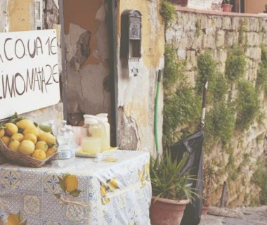 A table with lemons and lemonade in a narrow street with stone walls.