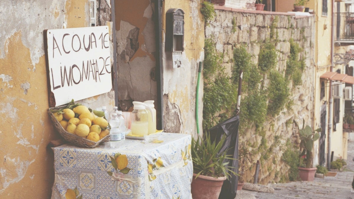 A table with lemons and lemonade in a narrow street with stone walls.